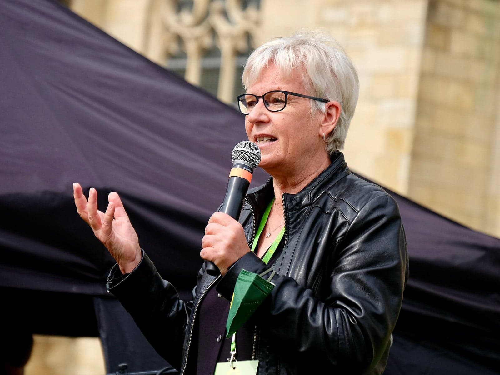 Maria Klein-Schmeink mit Mikrophon bei einer oeffentlichen Rede in schwarzer Lederjacke